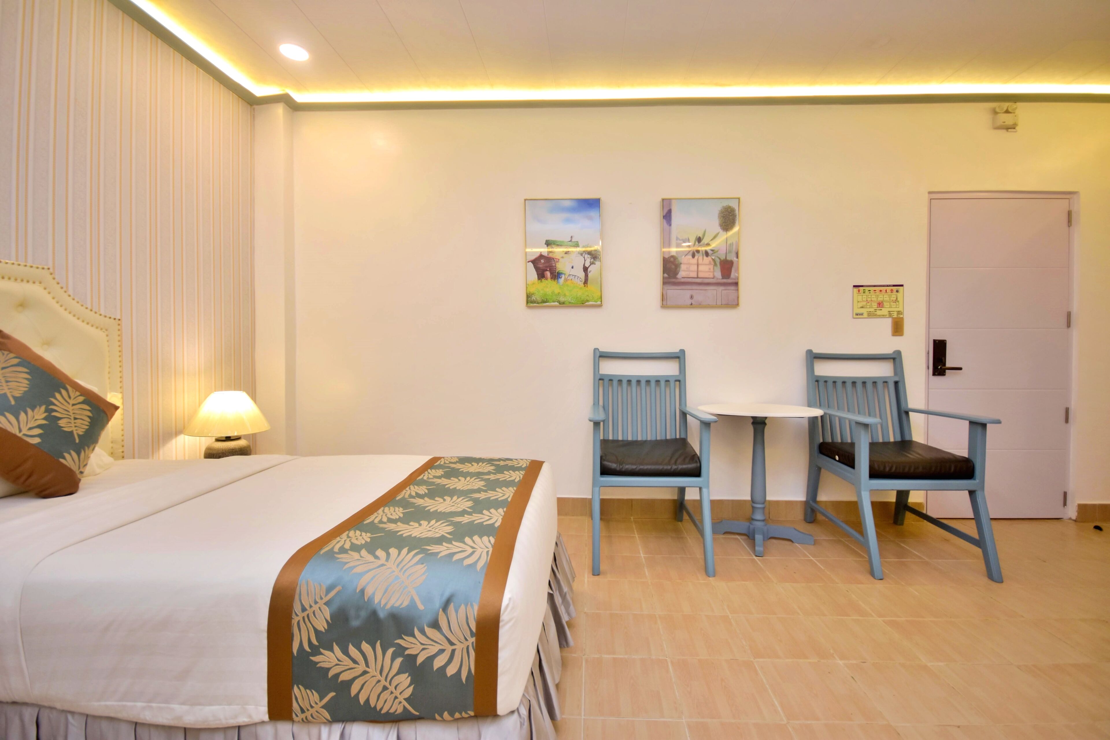 A hotel room with a bed, two chairs, a small table, and a door.