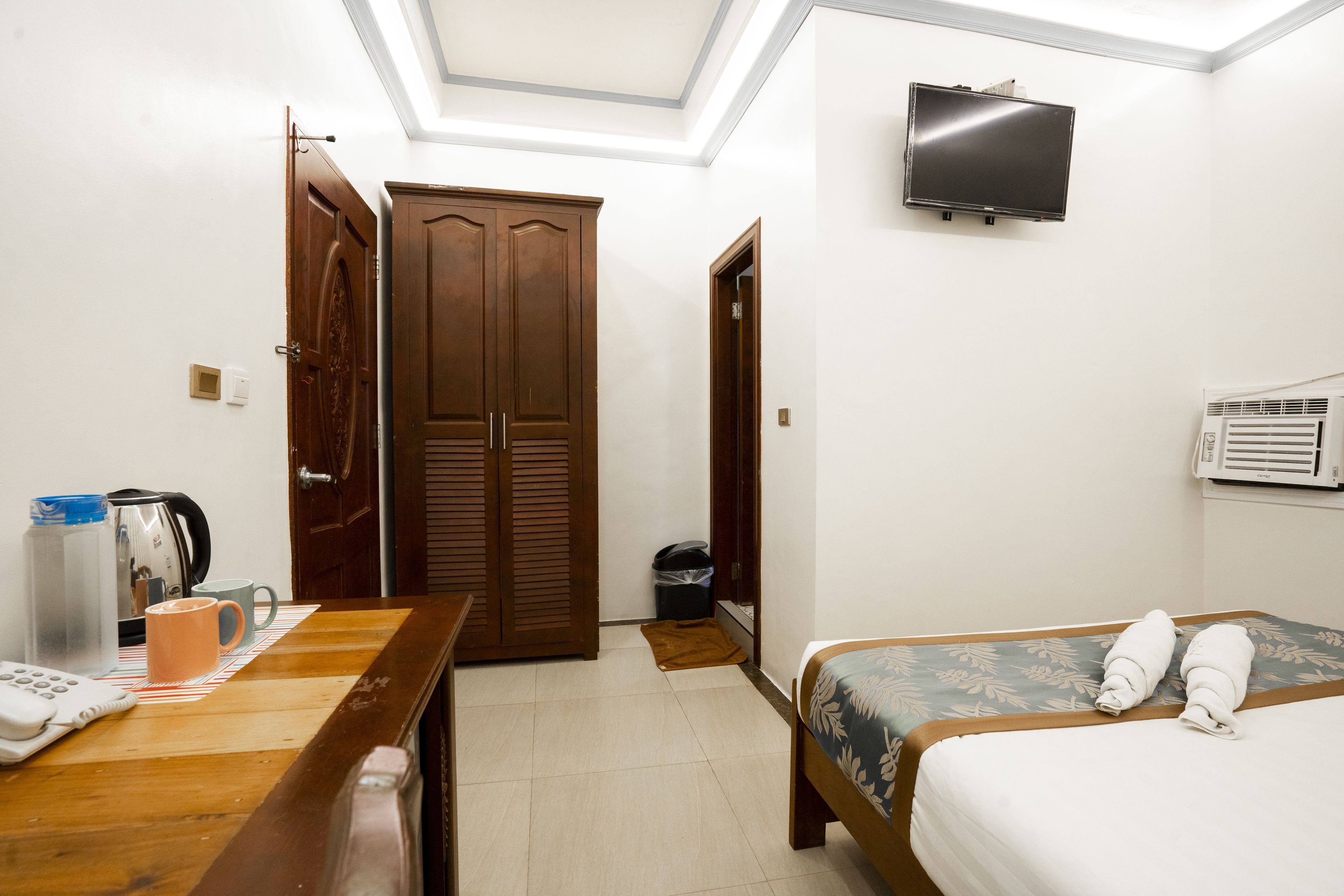 Une chambre d’hôtel avec un lit, un bureau doté d’une bouilloire, d’une machine à café et d’un téléviseur fixé au mur.
