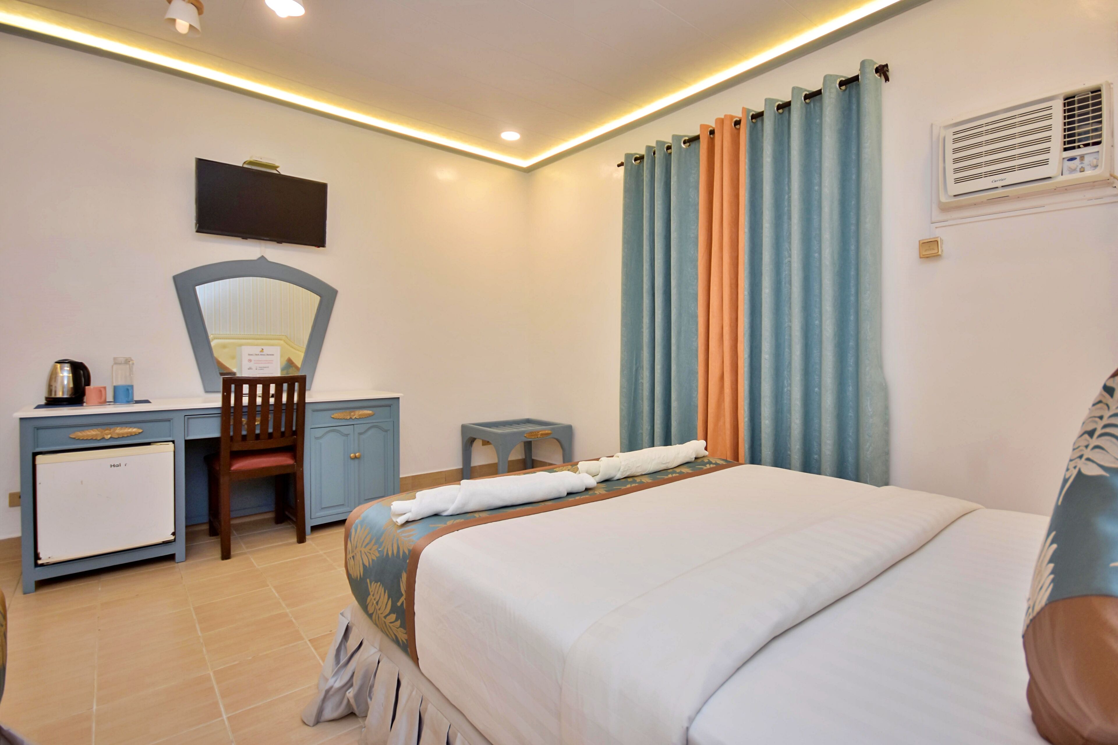 Habitación de hotel con cama, escritorio con silla, televisor y aire acondicionado.