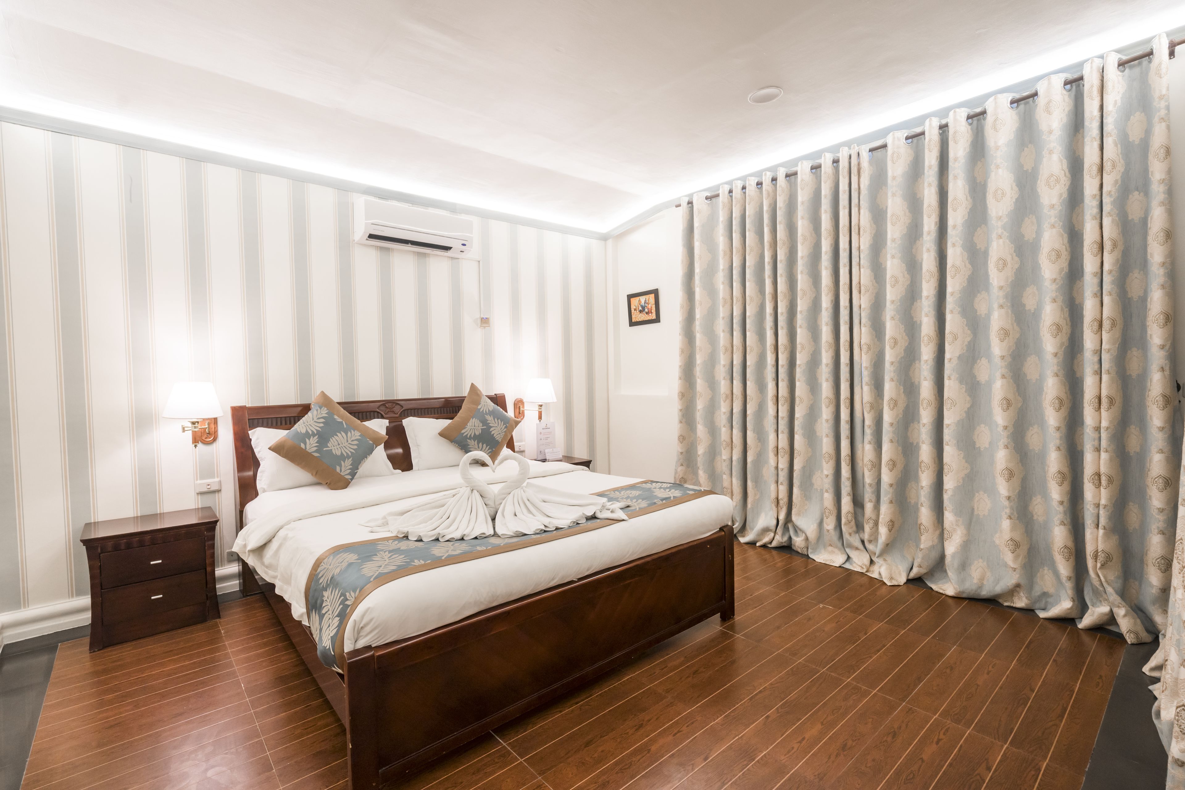 A neatly made bed with a heart-shaped towel, a wooden headboard, and a nightstand with a lamp.