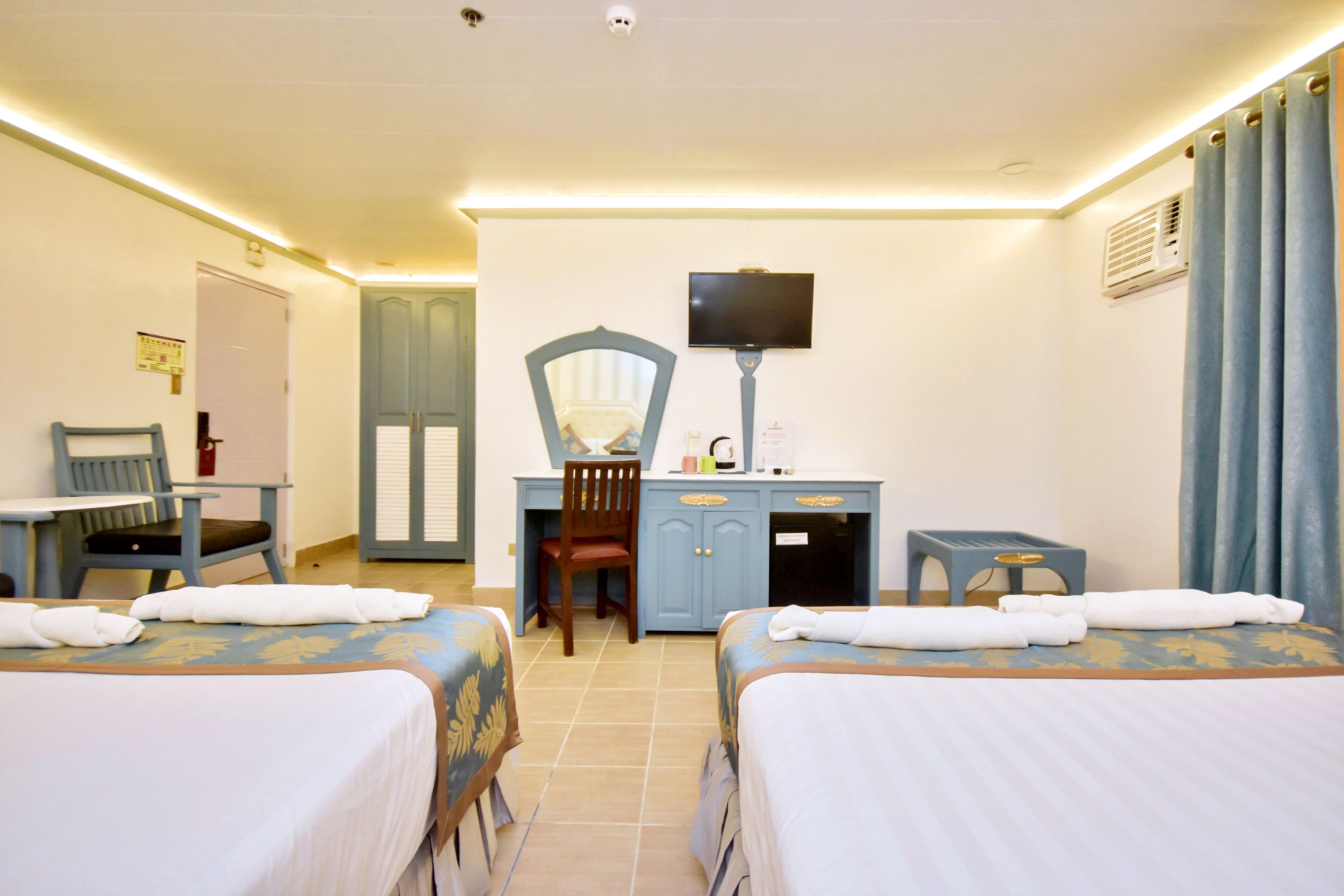 Habitación de hotel con dos camas, un escritorio con silla, un televisor y un taburete pequeño.
