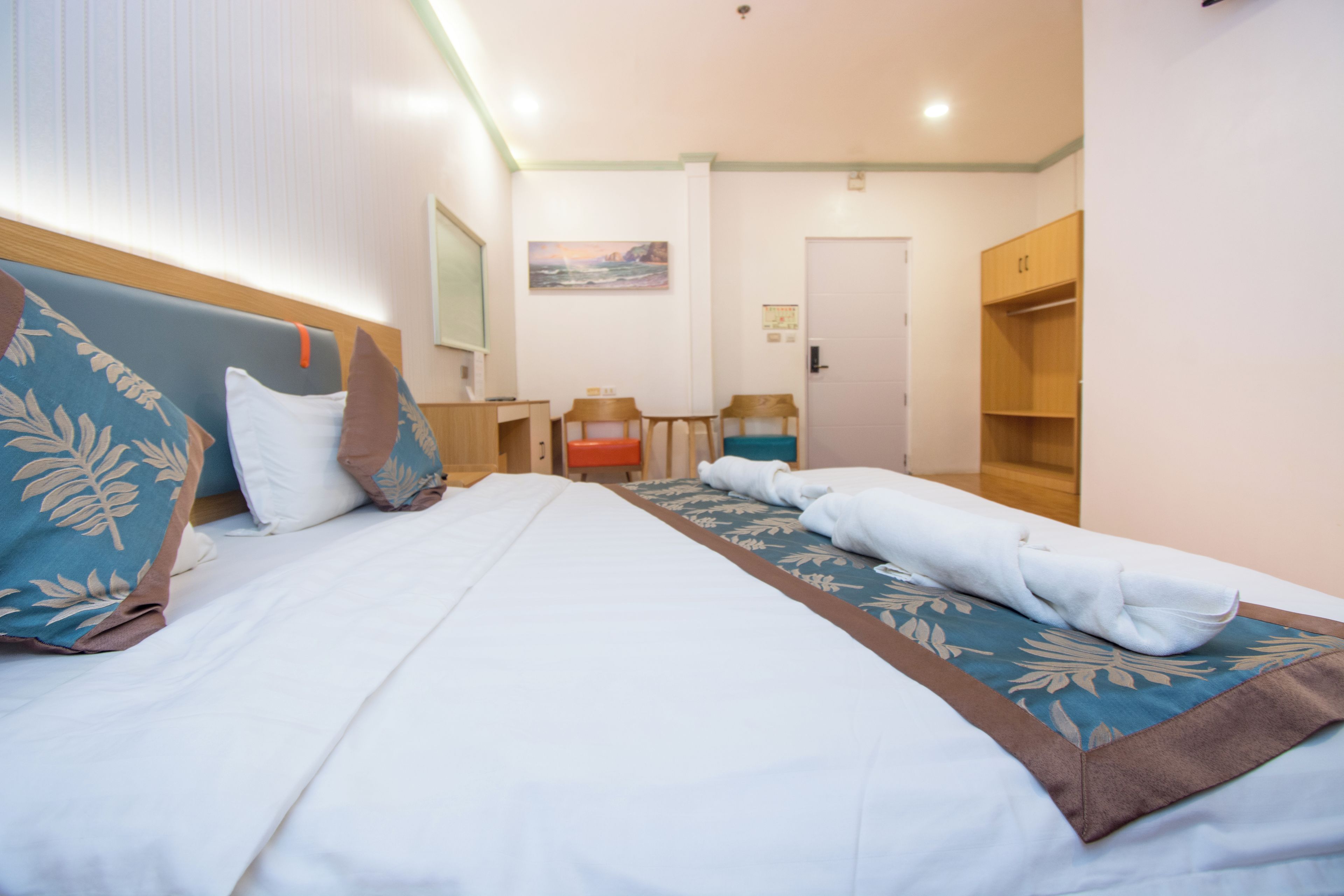Una habitación de hotel con cama, escritorio, silla, armario y un cuadro en la pared.