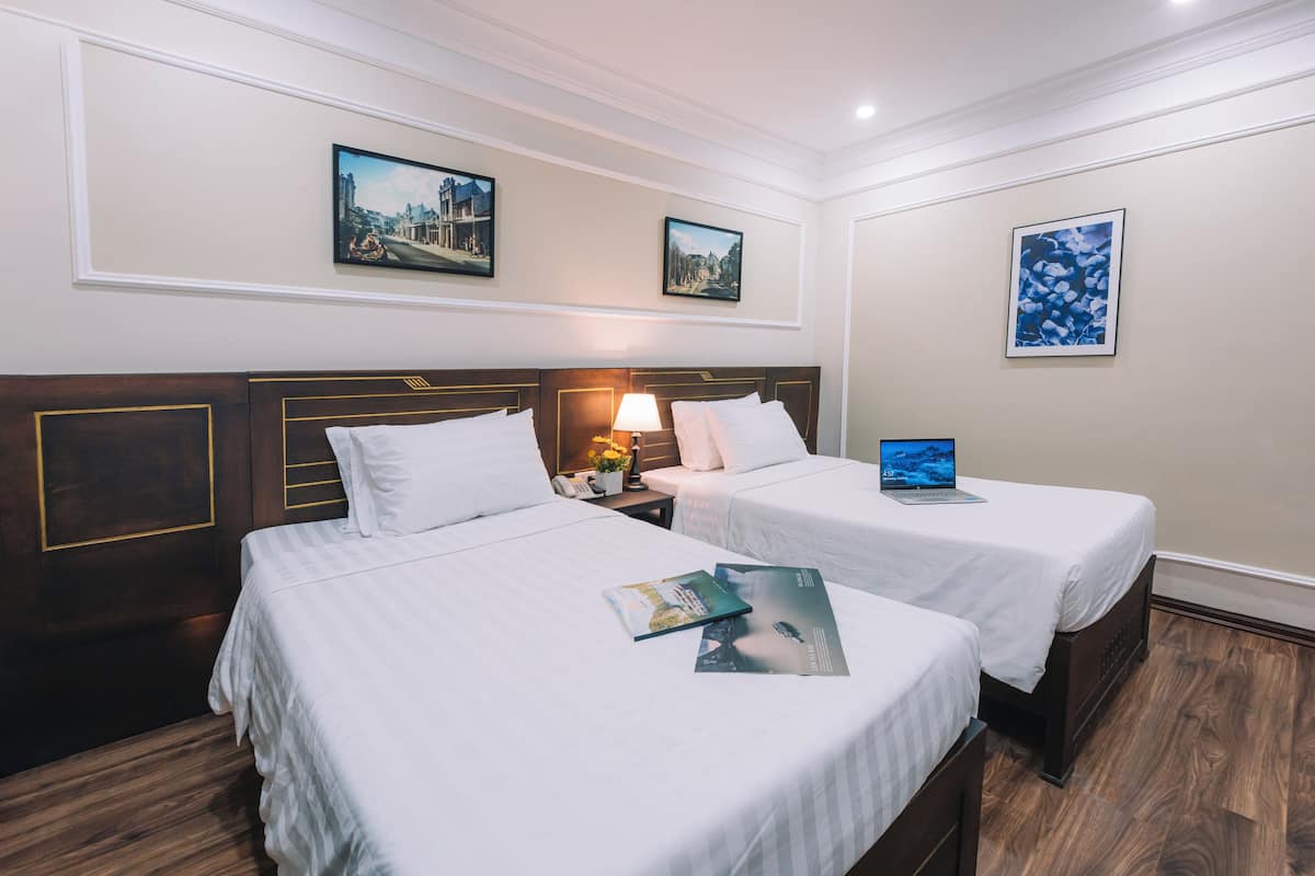 A hotel room with two beds, a nightstand with a lamp, and framed pictures on the walls.