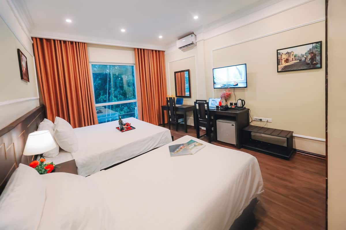 A hotel room with two beds, a desk with a computer, a TV, and a window with curtains.