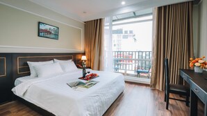 Habitación de hotel con una cama grande, un escritorio, una silla, un balcón con vistas y un cuadro en la pared.