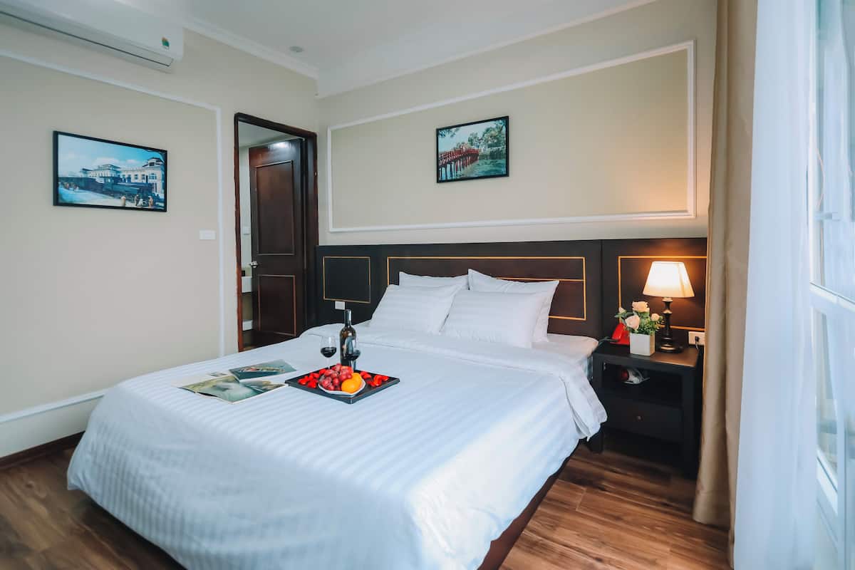 A hotel room with a neatly made bed, a bedside table with a lamp, and two framed pictures on the wall.