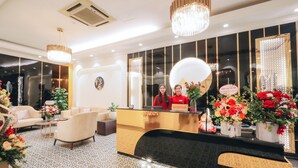 Zona de recepción de un hotel con un mostrador negro, dos recepcionistas con uniformes rojos y un candelabro.