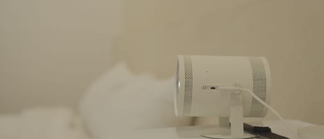 Un purificador de aire portátil blanco sobre una superficie blanca, con el cable de alimentación conectado.