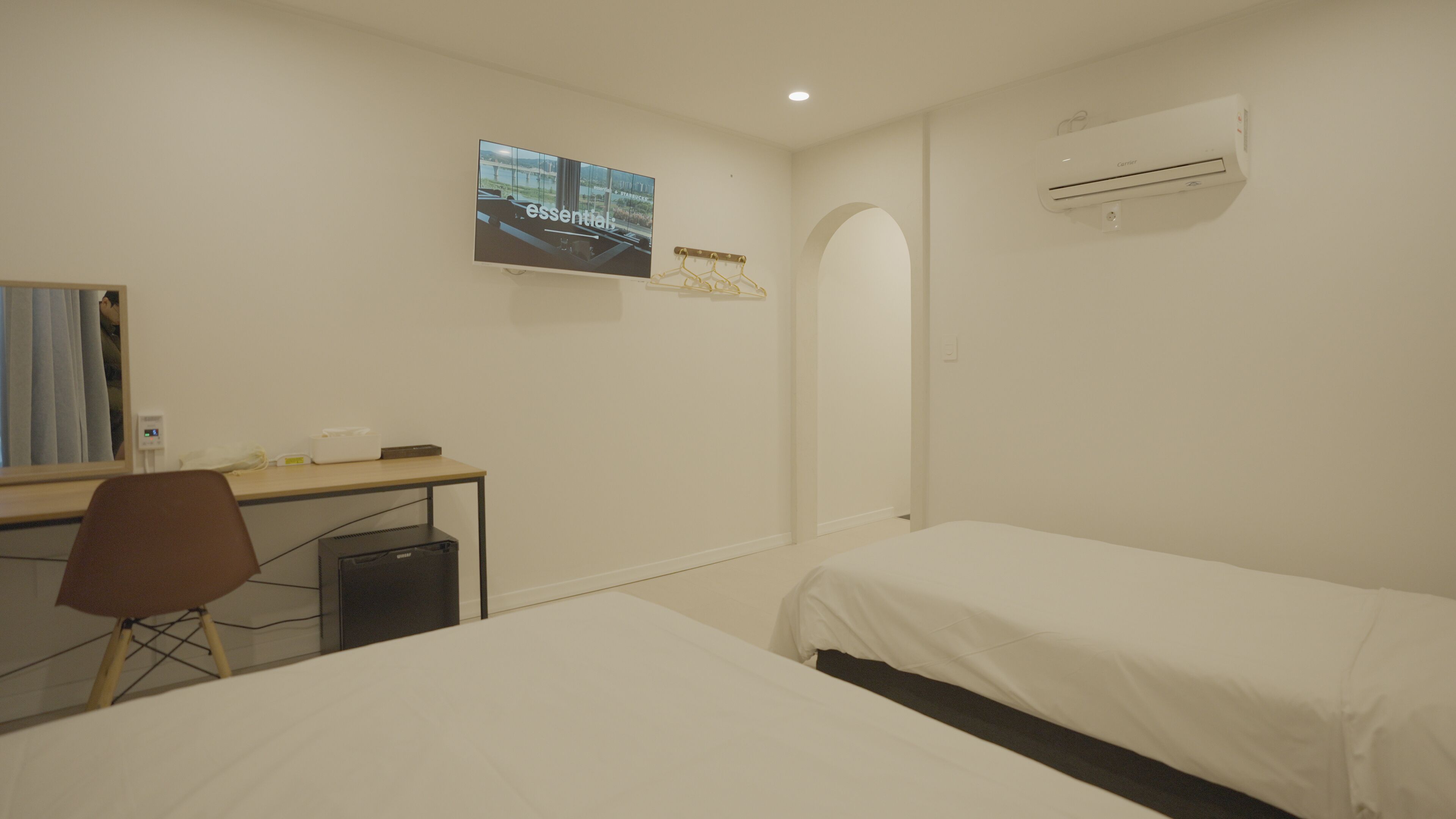 Habitación de hotel con cama, escritorio, silla, mesita pequeña, aire acondicionado y televisor montado en la pared.