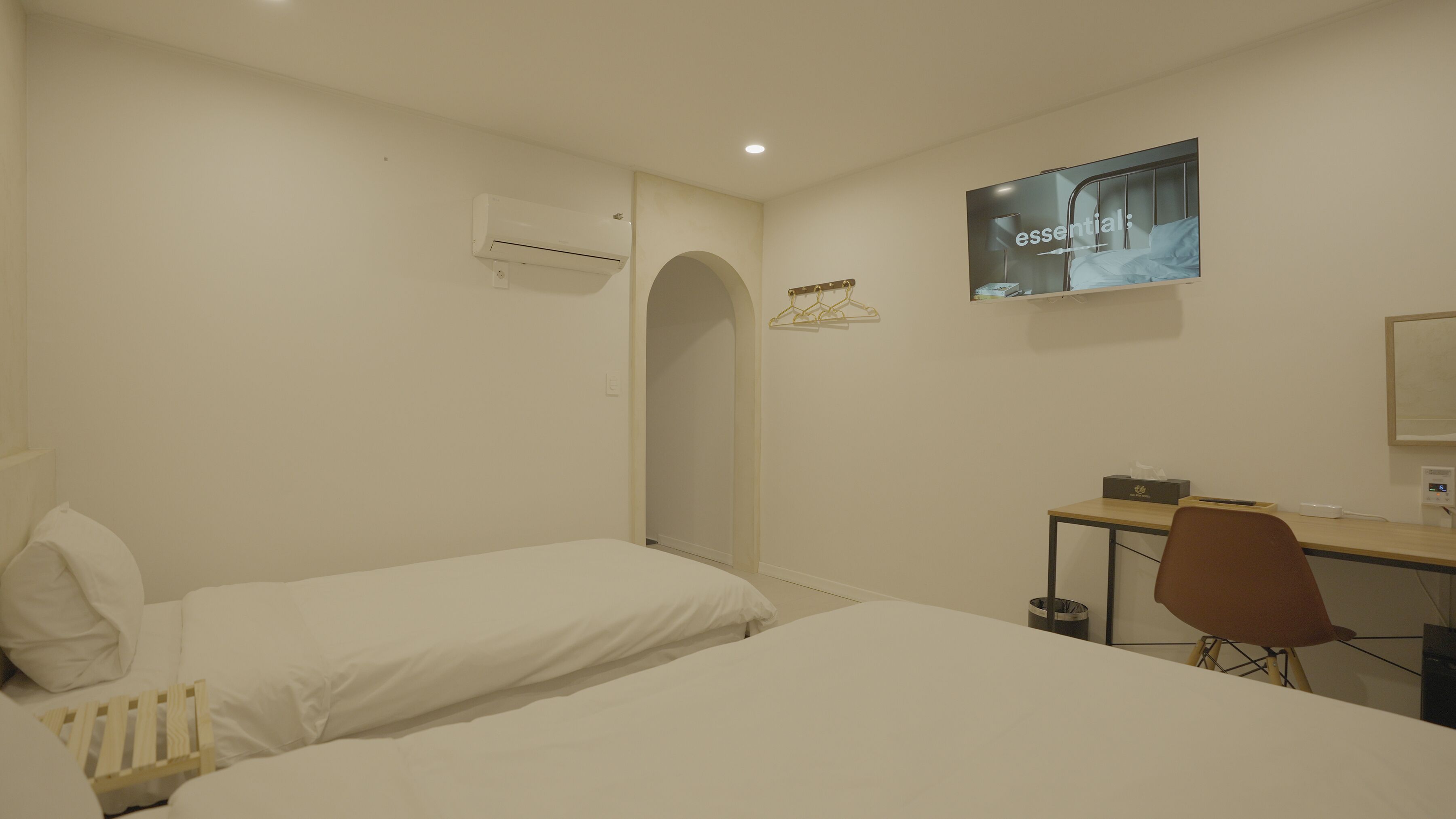 Hotelkamer met twee bedden, een bureau, een stoel, een airconditioning, een televisie en een kleine prullenbak.