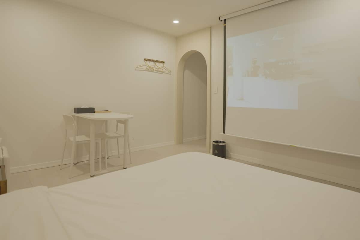 A minimalist hotel room with a bed, a small table, and a projector screen displaying a presentation.