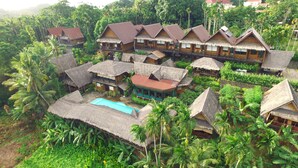 A resort with thatched-roof bungalows, a swimming pool, and lush tropical vegetation. - Palau Plantation Resort (Koror)