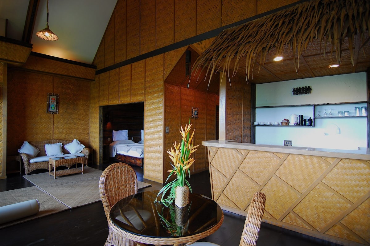 A room with a reception desk, a dining area with a round table and chairs, a sofa, and a decorative plant.