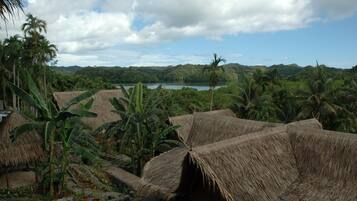 A tropical landscape with thatched-roof huts, lush greenery, and a lake in the background.