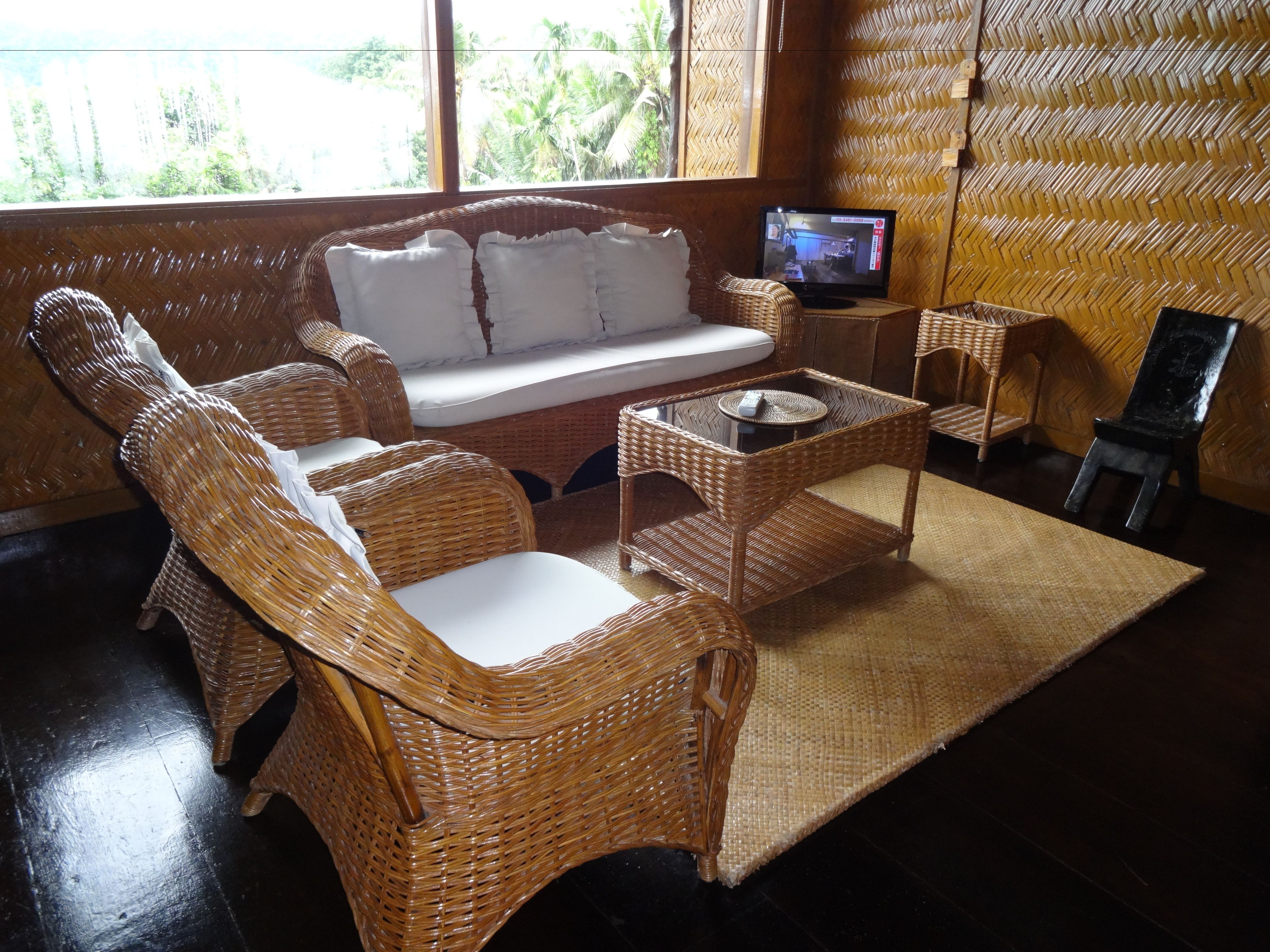 A room with wicker furniture, including a sofa and chairs, a small table, and a television on a stand.
