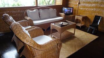 A room with wicker furniture, including a sofa and chairs, a small table, and a television on a stand.
