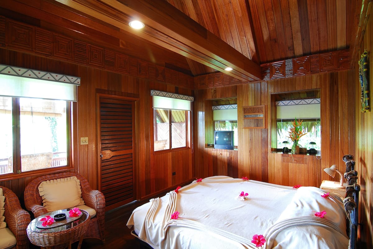 A wooden room with a bed, wicker chairs, and a television.