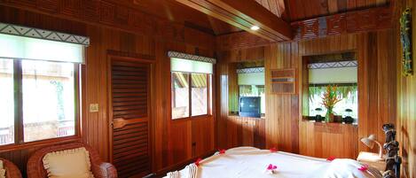 A wooden room with a bed, wicker chairs, and a television.
