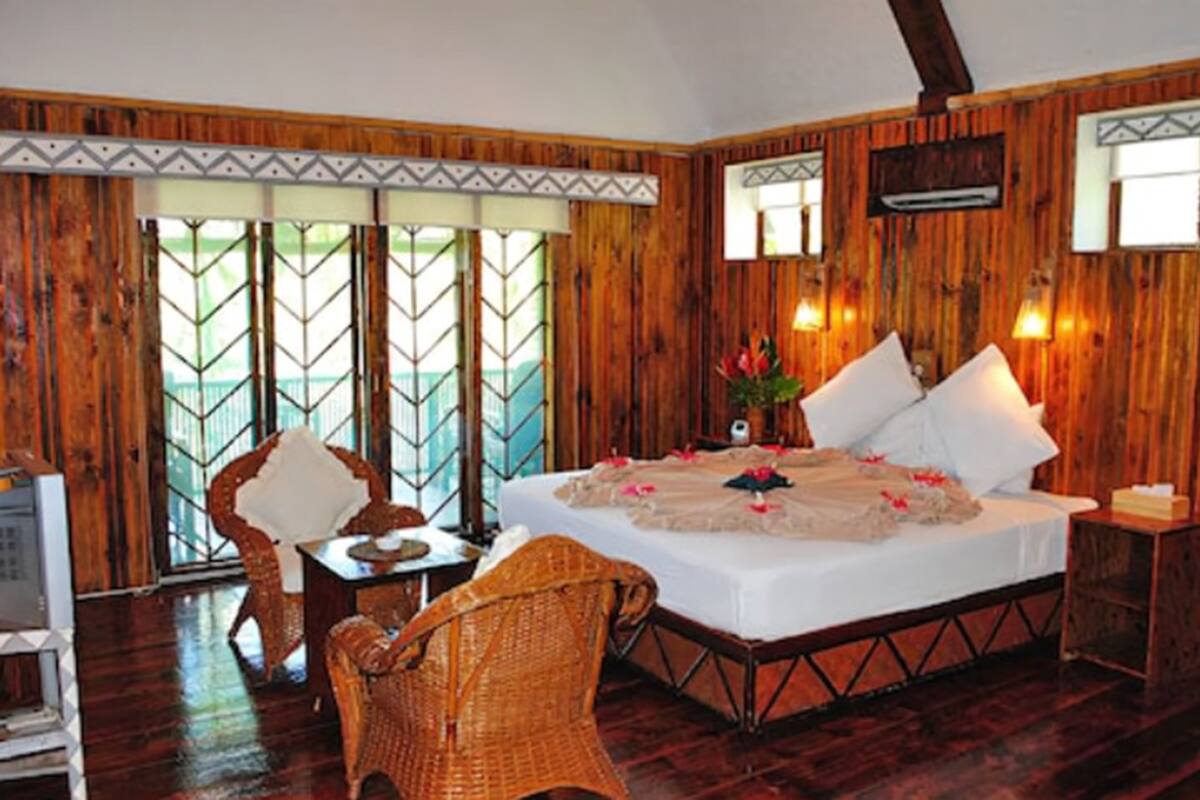 A wooden-paneled room with a bed, two wicker chairs, a small table, and a television.