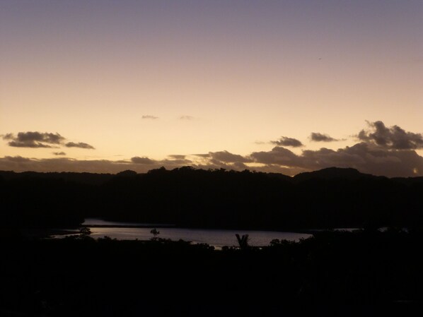 Silueta de un paisaje con un cuerpo de agua, árboles y colinas bajo un cielo crepuscular.
