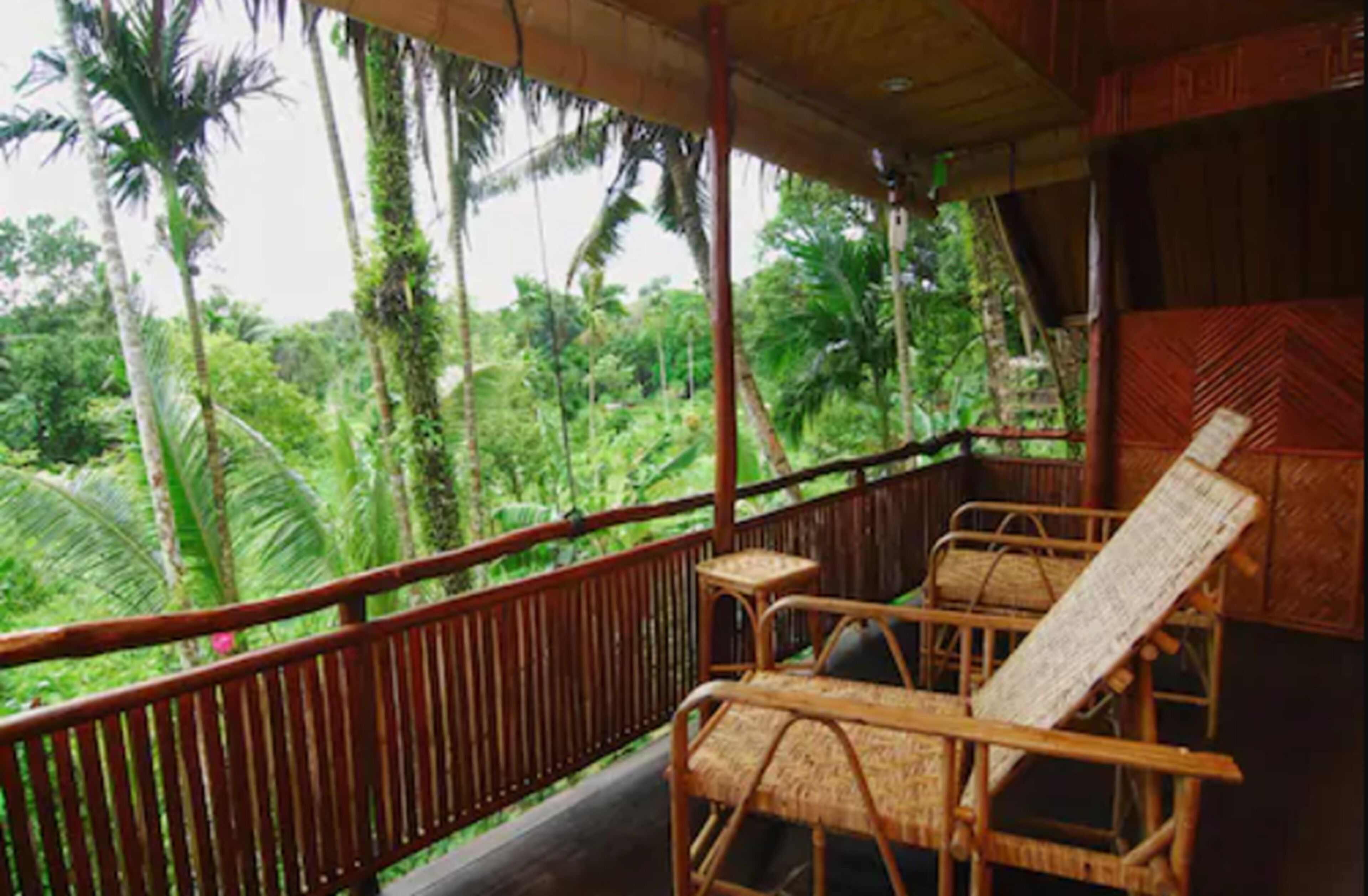 A wooden balcony with wicker furniture overlooking a lush tropical garden.