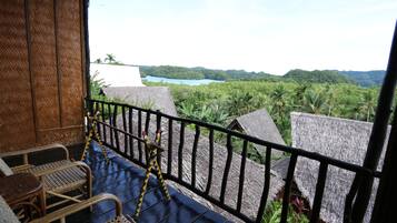 A balcony with wicker furniture, a metal railing, and a view of a lake surrounded by greenery.