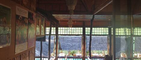 Interior con paredes de madera, techo de paja y vista a un cuerpo de agua.