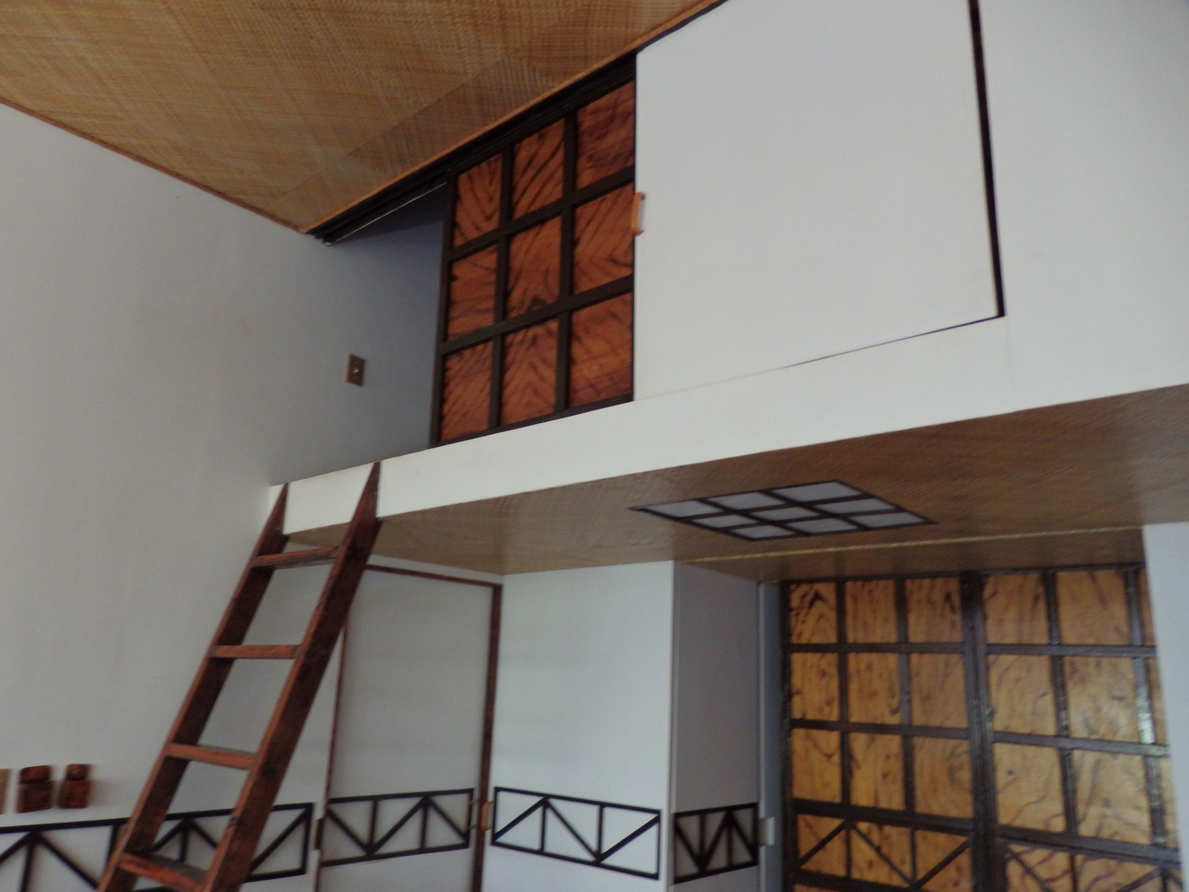 Ein Zimmer mit einer Holzleiter, einem Fenster mit Gittermuster und einer Tür mit geometrischem Design.