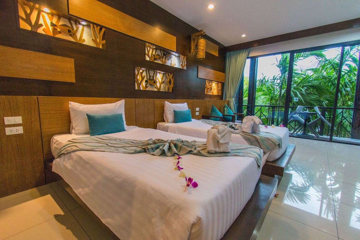 A hotel room with two beds, a balcony with a view of tropical foliage, and a modern decor style.