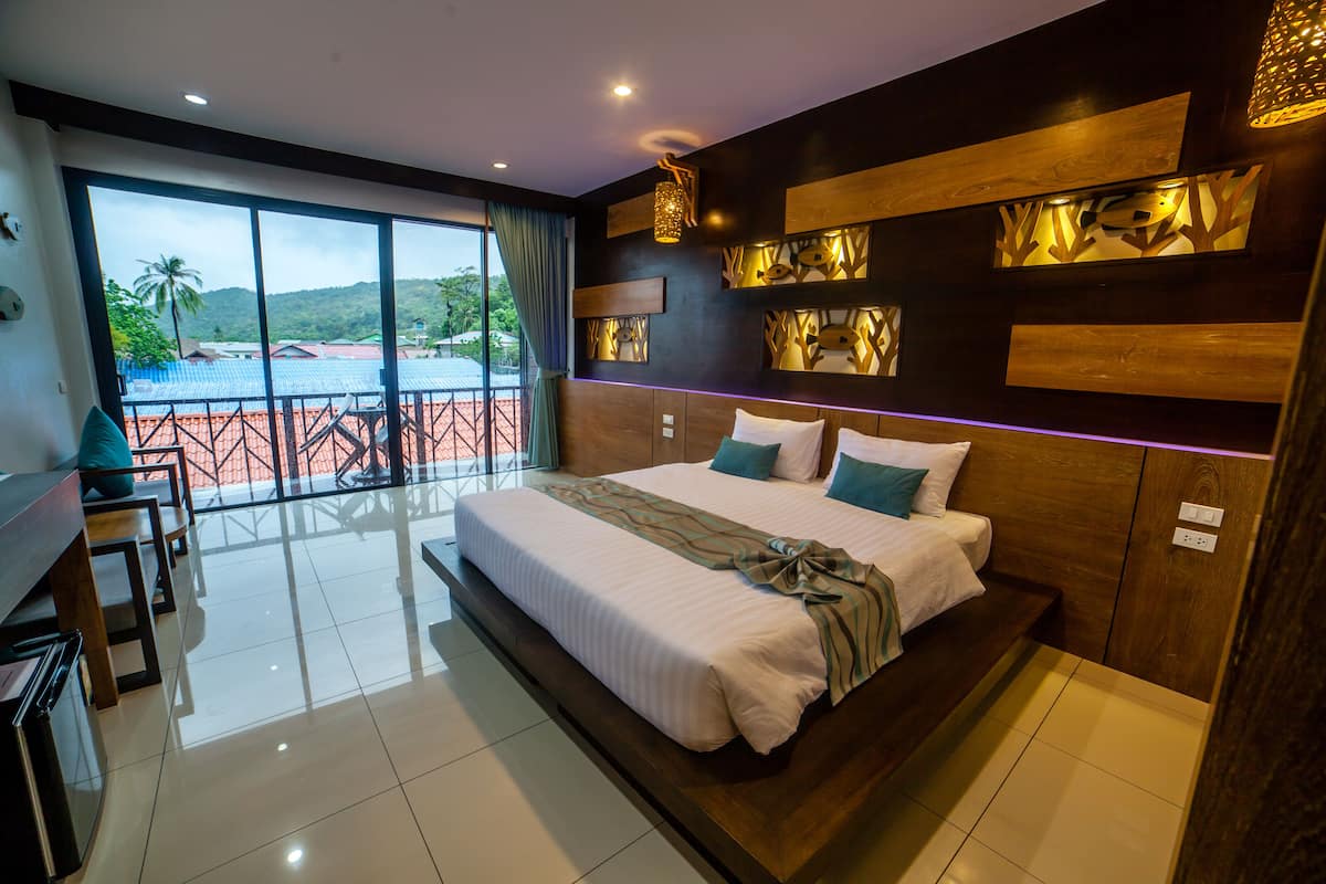 A modern hotel room with a large bed, a balcony with a view of the mountains, and a dining area with a view.