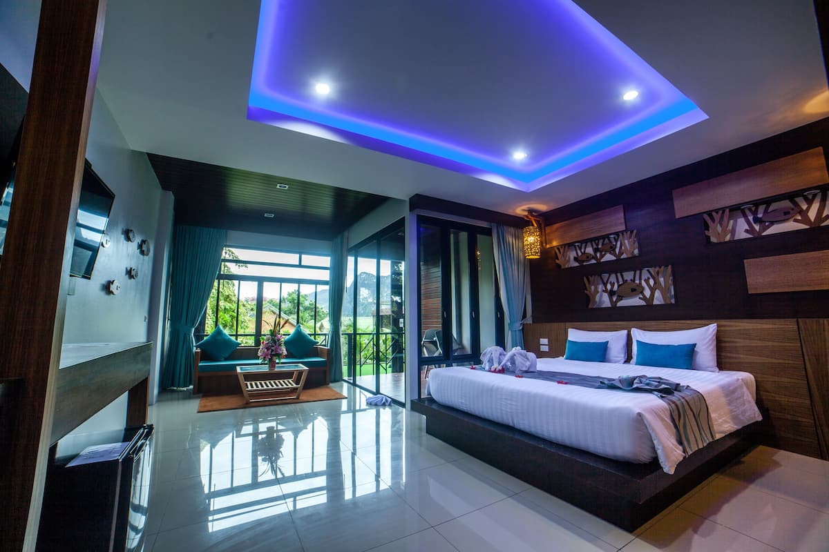 A modern hotel room with a large bed, a seating area with a view, and a ceiling with blue lighting.