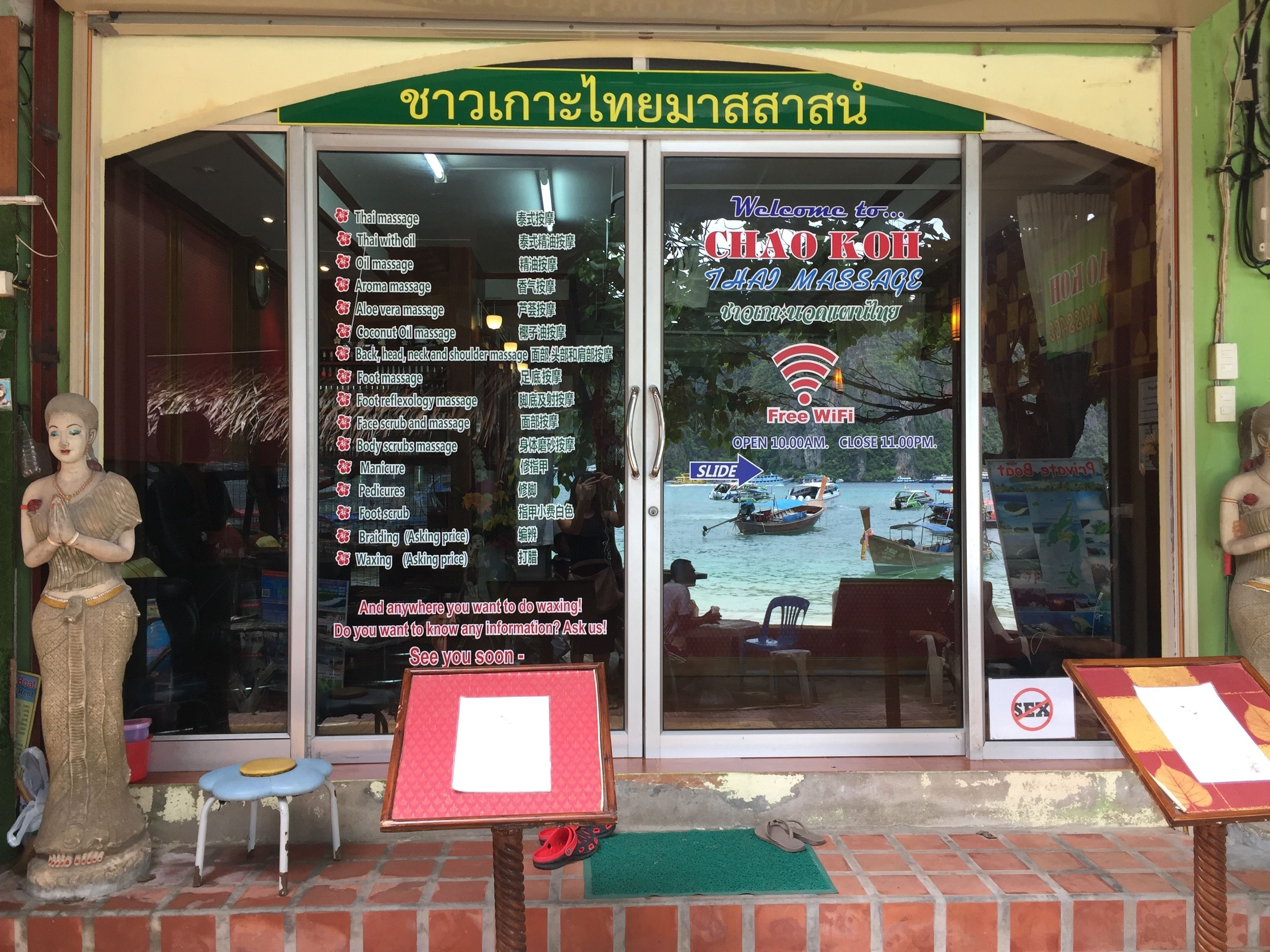 A massage parlor with a list of services on the glass door, including Thai massage and aromatherapy.