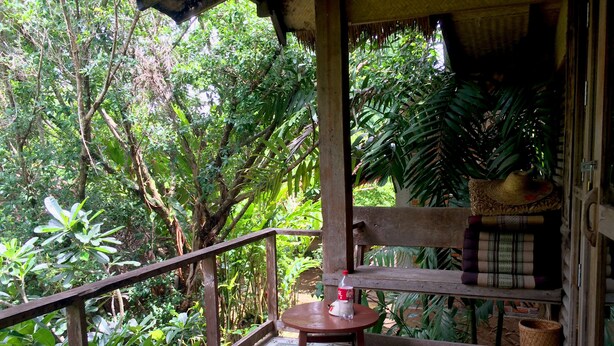 A wooden deck with a table and chairs, surrounded by lush greenery. - Sipsongpanna Resort Pai (Pai)