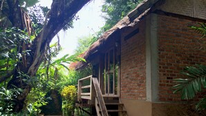 A rustic building with a brick exterior, a wooden staircase leading to a balcony, surrounded by lush greenery. - Sipsongpanna Resort Pai (Pai)