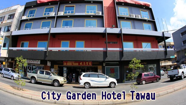 En byggnad med flera våningar, en röd och grå fasad, många fönster och en skylt med texten City Garden Hotel Tawau.