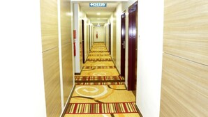 En hotellkorridor med ett mönstrat golv, träpanel på väggarna och dörrar som leder till rummen.