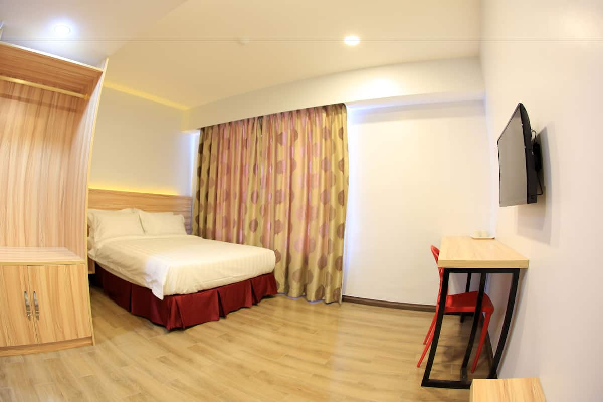 Ein Hotelzimmer mit Bett, Schreibtisch, Stuhl und einem an der Wand befestigten Fernseher.