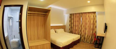 Habitación de hotel con cama, armario de madera, escritorio con silla y zona de ducha.