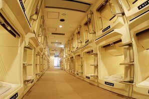 A hotel corridor with rows of single beds, each with a small window and a door. - Capsule Hotel Wellbe Sakae - Caters to Men (Nagoya)