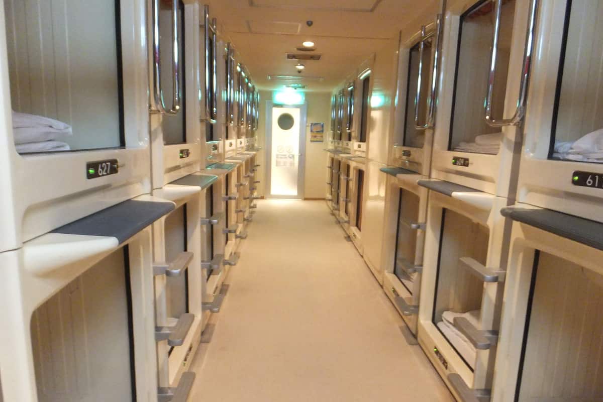A hotel corridor with rows of individual rooms, each equipped with a bed and a window.