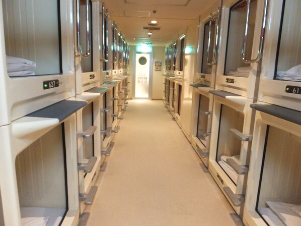 A hotel corridor with rows of individual rooms, each equipped with a bed and a window. - Capsule Hotel Wellbe Sakae - Caters to Men (Nagoya)