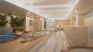 A large indoor swimming pool with multiple lanes, surrounded by tiled walls and a wooden ceiling. - Capsule Hotel Wellbe Sakae - Caters to Men (Nagoya)