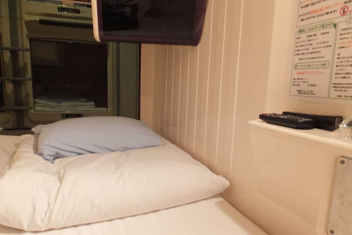 A hotel room with a bed, a television mounted on the wall, and a window with blinds.