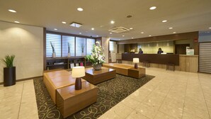 A hotel reception area with a reception desk, seating area, and potted plants. - Hotel Resol Machida (Machida)