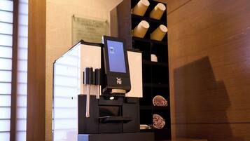 A coffee machine with a digital display, a coffee grinder, and a shelf with cups.