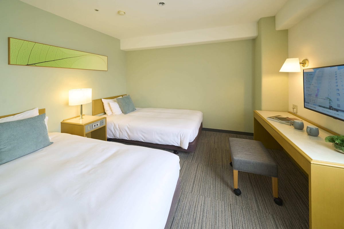 A hotel room with two beds, a desk, a chair, a TV, and a map on the wall.