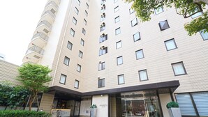 A modern hotel entrance with a glass facade, a landscaped area with a tree, and a sign indicating the hotel name. - Hotel Resol Machida (Machida)
