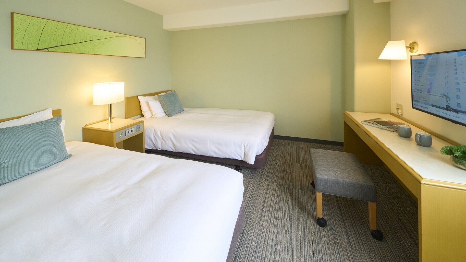A hotel room with two beds, a desk, a chair, a TV, and a map on the wall.
