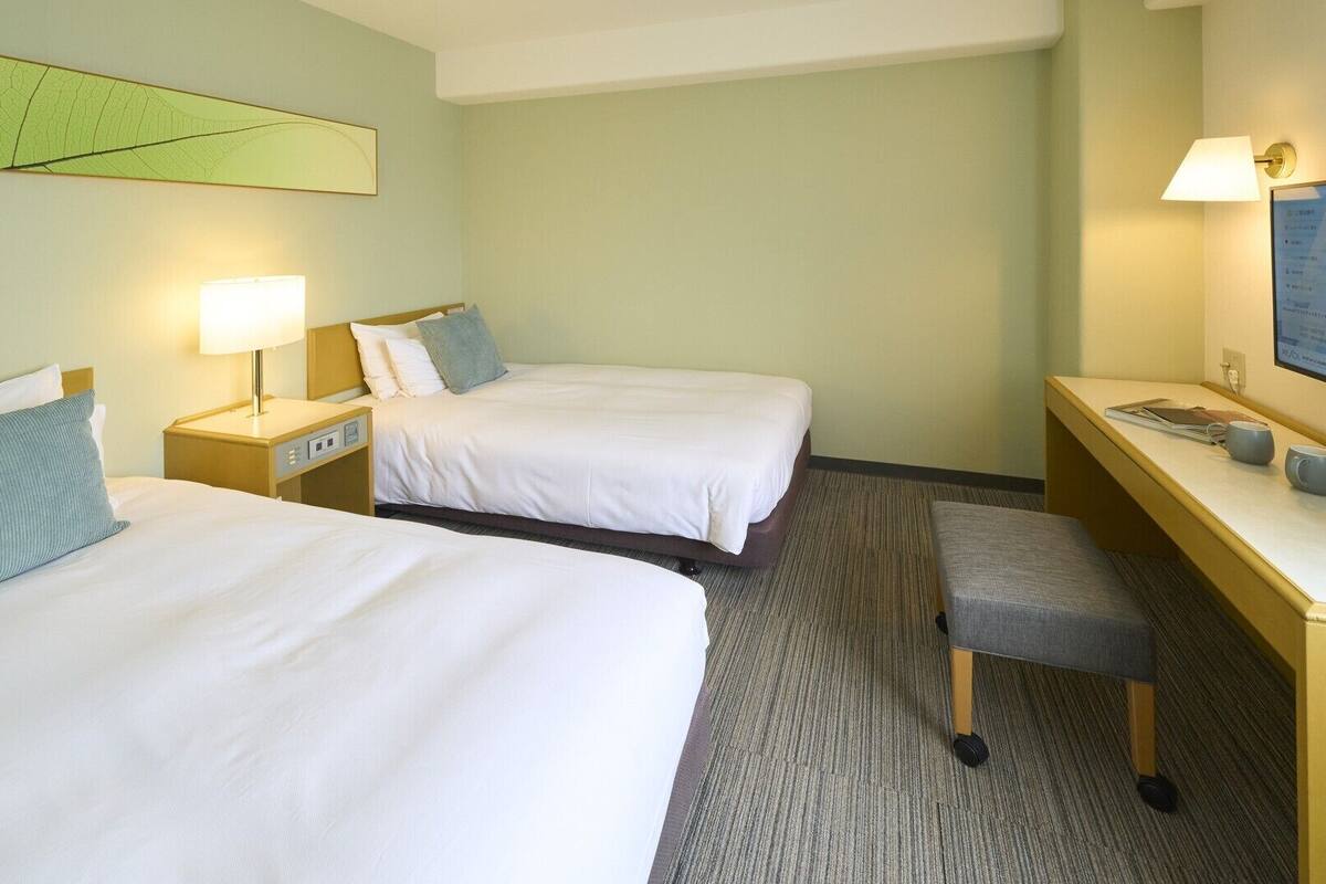 A hotel room with two beds, a desk, a chair, a TV, and a map on the wall.
