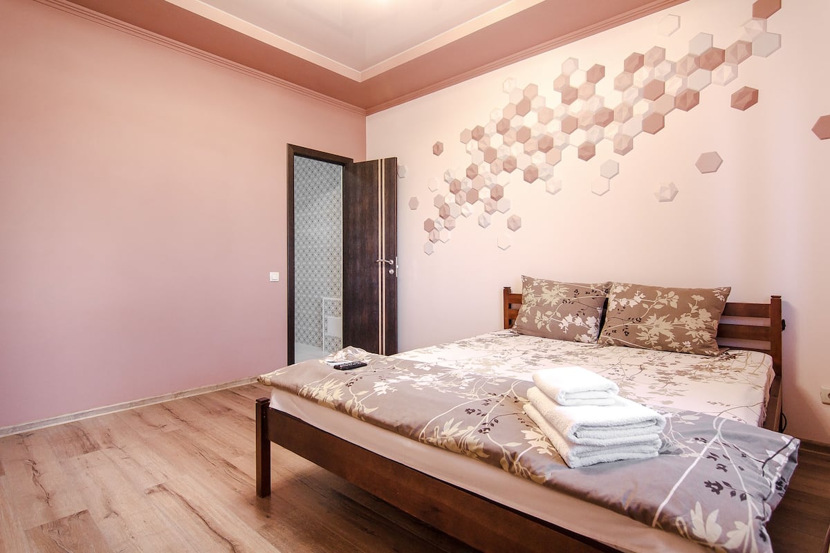Une chambre à coucher avec un lit en bois, un mur orné de motifs hexagonaux et une porte dotée d’un panneau de verre décoratif.